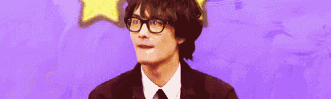 a man wearing glasses and a suit and tie is standing in front of a purple wall .