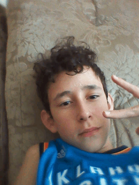 a young man laying on a bed wearing a blue shirt that says klah on it
