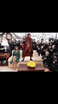 a woman sits on a couch while a man in a superhero costume stands next to her