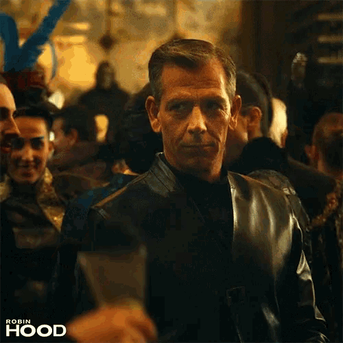 a man in a leather jacket is standing in a crowd with robin hood written on the bottom right