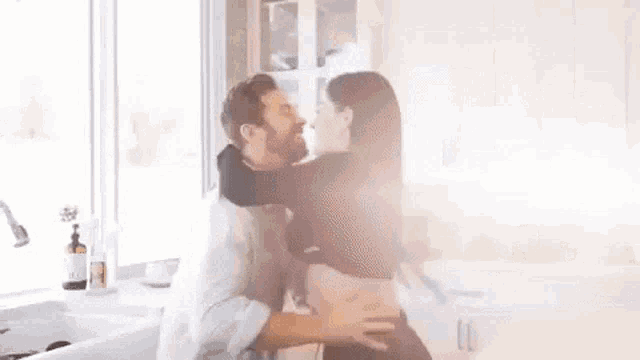 a man is holding a woman in his arms in a kitchen and kissing her .