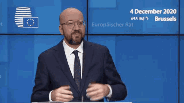 a man in a suit and tie is standing in front of a screen with the date 4 december 2020 on it .