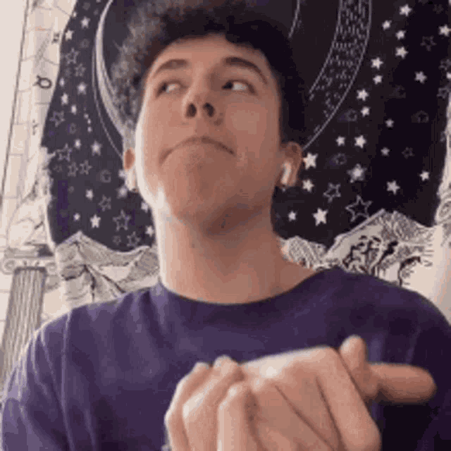 a young man in a purple shirt is clapping his hands in front of a wall tapestry .