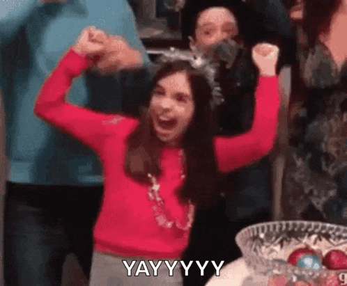 a girl in a red sweater is raising her arms in the air and laughing .