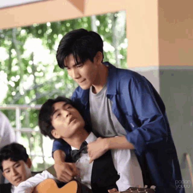 a man in a blue jacket is hugging another man in a bow tie while holding a guitar