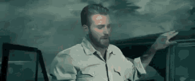 a man with a beard is standing in front of a car and pointing .