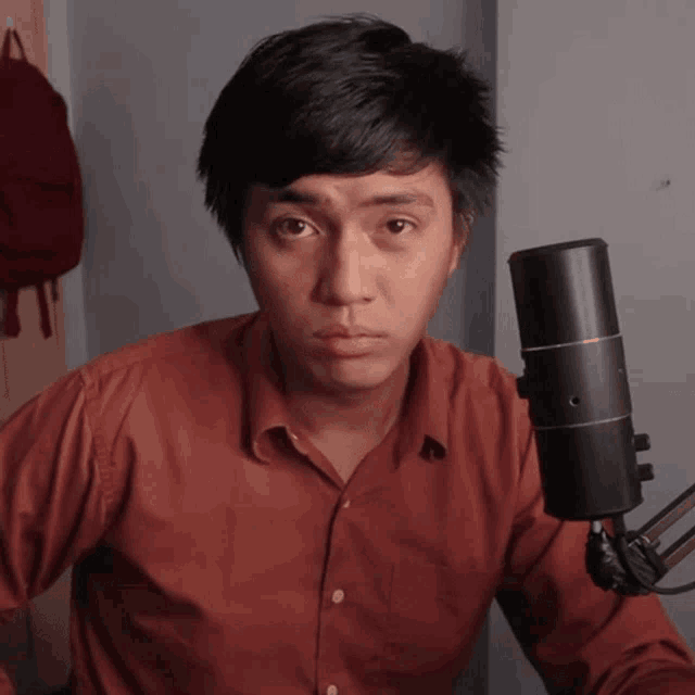 a young man in a red shirt stands in front of a microphone