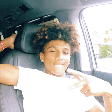 a young man with curly hair is sitting in a car and giving a thumbs up