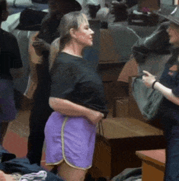 a woman in a black shirt and purple shorts is standing in a room with other people