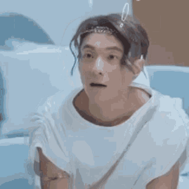 a man in a white toga is sitting on a couch and making a surprised face .
