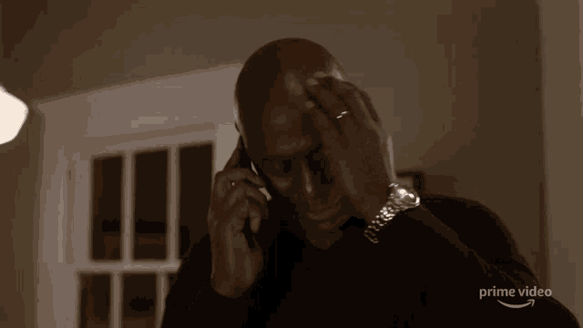 a man wearing a watch is talking on a cell phone with a prime video logo behind him