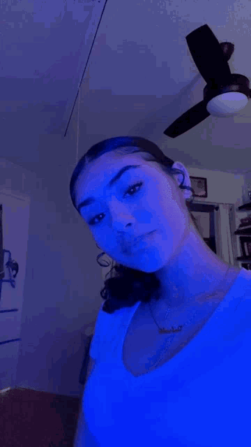 a girl is taking a selfie in a room with a ceiling fan and blue lights .