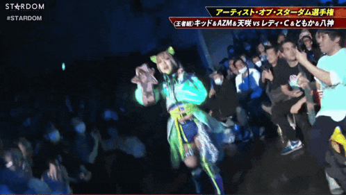 a woman in a green and yellow outfit is dancing in front of a crowd with the word stardom on the bottom right