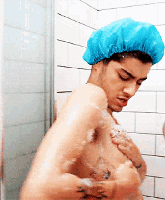 a man taking a shower with a blue shower cap on his head