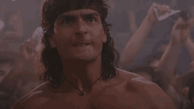 a shirtless man with long hair and a necklace looks up