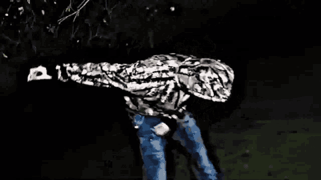 a man in a camo jacket and jeans is standing in the dark