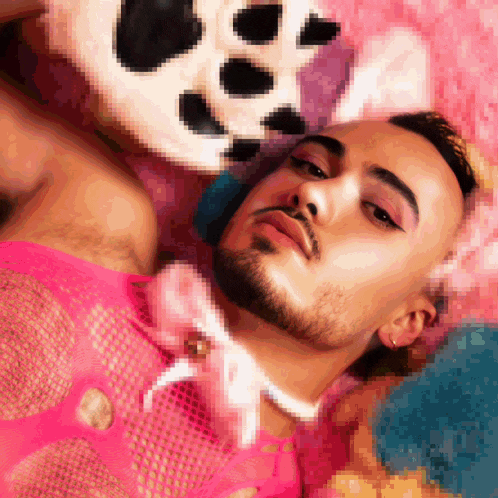a pixelated image of a man laying on a bed with a stuffed animal in the background