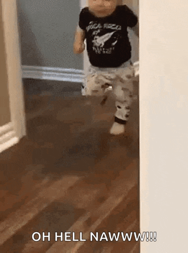 a baby is walking across a wooden floor in a hallway .