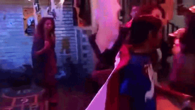 a group of people are dancing in a room with a purple light behind them