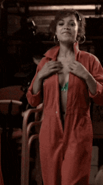 a woman in a green bra and red jumpsuit is taking off her shirt