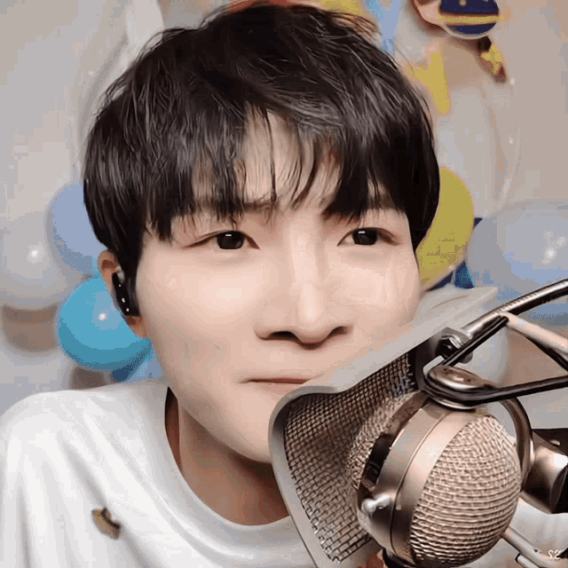 a close up of a person 's face behind a microphone with balloons in the background