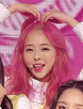a woman with pink hair is making a heart shape with her hands on her head .