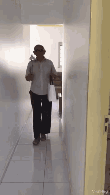 a man is walking down a hallway holding a white bag and a cane