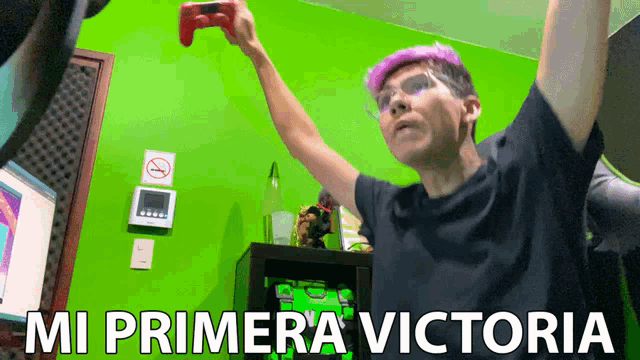 a man with purple hair is holding a video game controller in front of a green wall with the words mi primera victoria