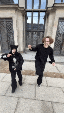 a man and a woman are holding hands in front of a building .