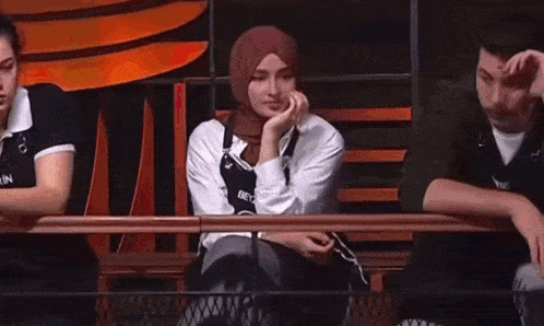 a woman in a hijab is sitting on a bench next to a man and a woman .