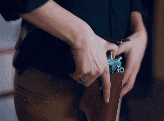 a person is putting a gun in their belt