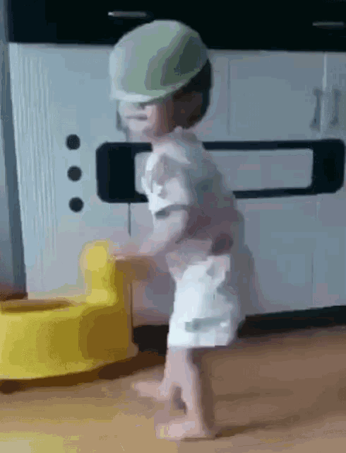 a little boy wearing a green hard hat is standing next to a yellow potty