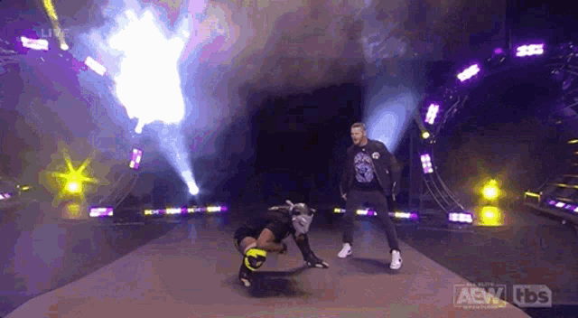 two wrestlers are standing on a stage with a fire coming out of the ceiling .