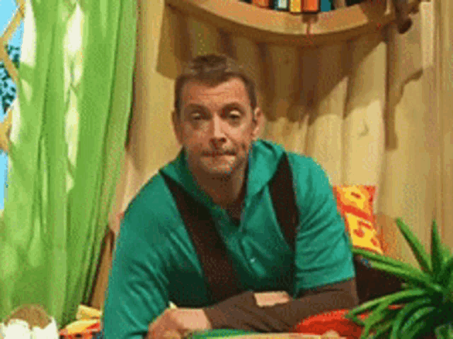 a man in a green shirt is sitting at a table in a room .
