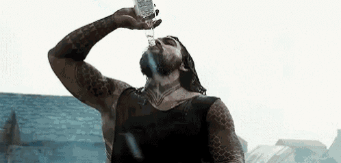 a man is drinking water from a bottle while standing next to a body of water .