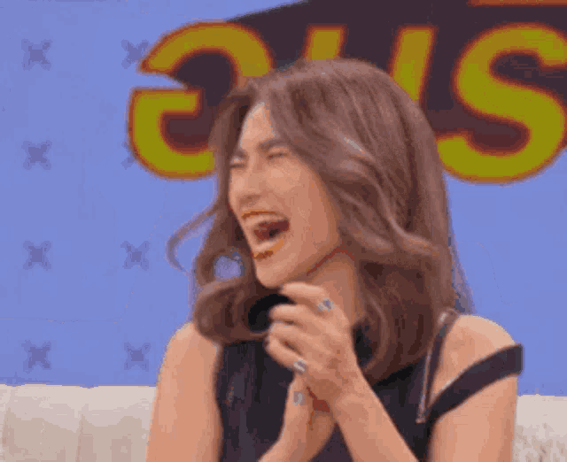 a woman is laughing while sitting on a couch in front of a sign that says " s "