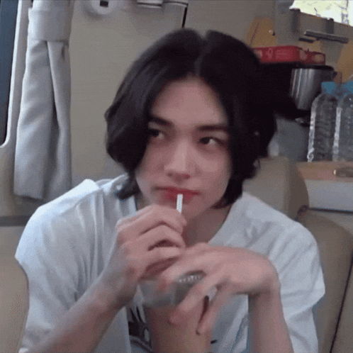 a young man with long hair is drinking a drink through a straw .