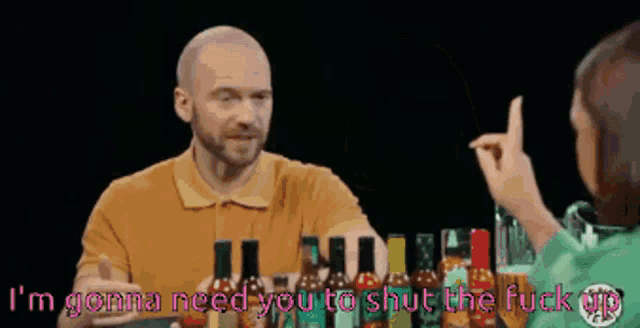 a man is talking to a woman while holding a bottle of hot sauce in front of him