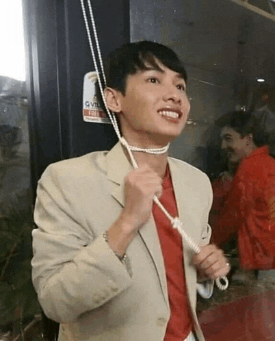 a young man in a suit and red shirt is holding a rope around his neck .