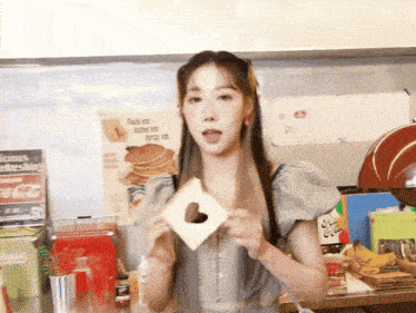 a woman holds a piece of bread with a heart cut out of it in front of a coca cola sign