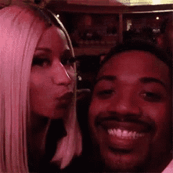 a man and a woman are posing for a picture and the woman is blowing a kiss at the man 's face .