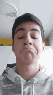 a young man with his eyes closed is wearing a grey hoodie