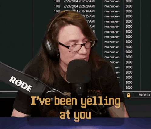 a woman wearing glasses and headphones is talking into a microphone with a sign that says drink water you bastard