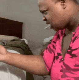a man wearing a pink camo shirt is standing in a bedroom .