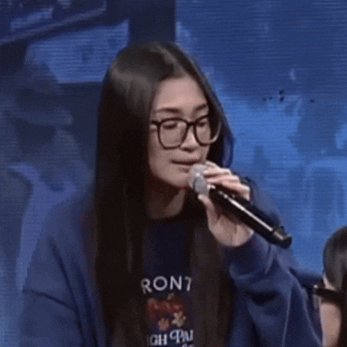 a woman wearing glasses and a blue sweatshirt is holding a microphone and says hello ?