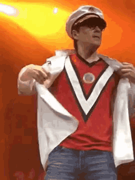 a man is wearing a captain 's hat and sunglasses while taking off his shirt .