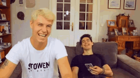 two men are sitting on a couch with one wearing a shirt that says stowen on it