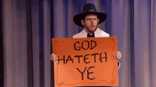 a man in a pilgrim hat holds an orange sign that says god hateth ye