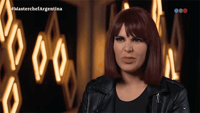 a woman with red hair and a black leather jacket is on a television screen that says masterchef argentina