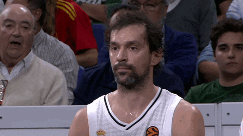 a man wearing a white jersey with a basketball on it sits in the stands